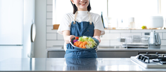 キッチンでカメラ目線のエプロンをつけた若い日本人女性