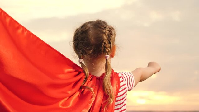 Girl stands with red cape billowing in wind as imagined as mighty Superwoman