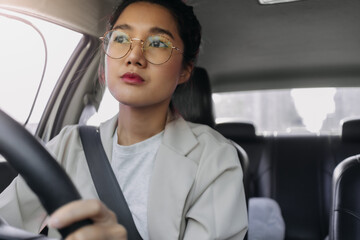 Front view of asian Thai woman wear eye glasses, driving car alone on road while going to work in the morning.