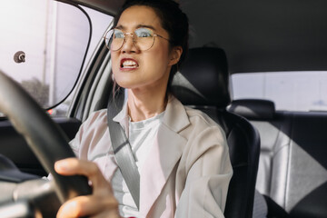 Asian woman wear eye glasses, got high temperature while driving a car on road, got mad angry with bad traffic in the morning, going to work.