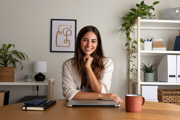 Young female entrepreneur at home office. Woman looking at camera sitting at desk.