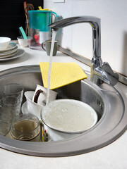 Close-up of a kitchen sink with dirty dishes. Water flows from an open tap. Reluctance to do routine housework.