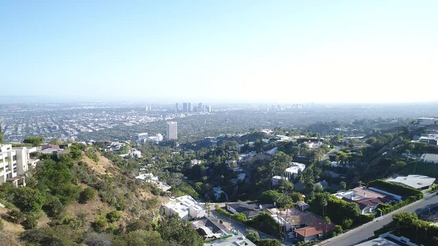 Drone shot of houses on Crescent Dr on a sunny day with Los Angeles skyline in the background, USA