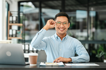 Obraz premium Middle-age Asian businessman smiles while looking at a laptop, possibly working as a Market Researcher or Marketing Analyst.