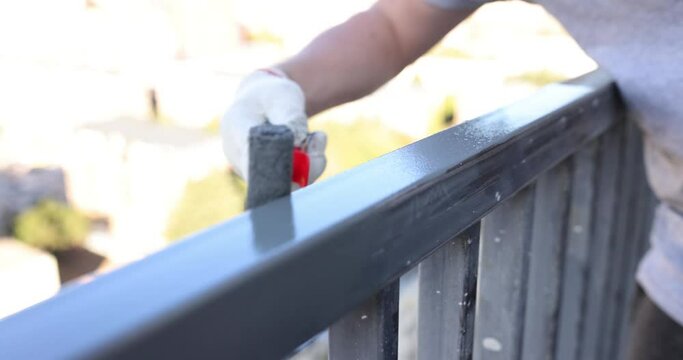 Man paints metal railing with gray paint closeup outdoors