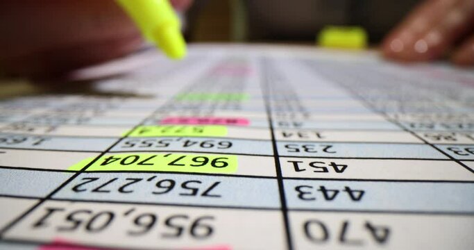 Paperwork and hand making notes with pink and yellow marker on sheet of paper of financial numerical data