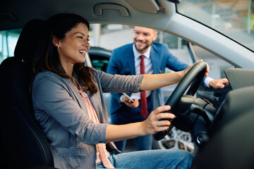 Happy woman testing new car in showroom.