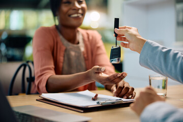 Close up of black woman receiving car key from salesperson in showroom.