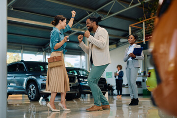 Cheerful couple dancing after buying new car in showroom.