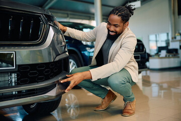 Happy black man examining new car in showroom.
