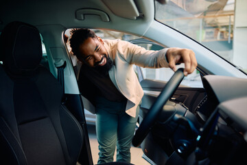 Happy black man buying new car in showroom.