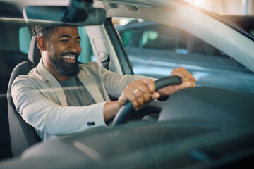Happy black man testing new car in showroom.