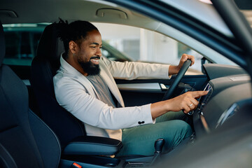 Happy black man inside of new vehicle at car dealership.