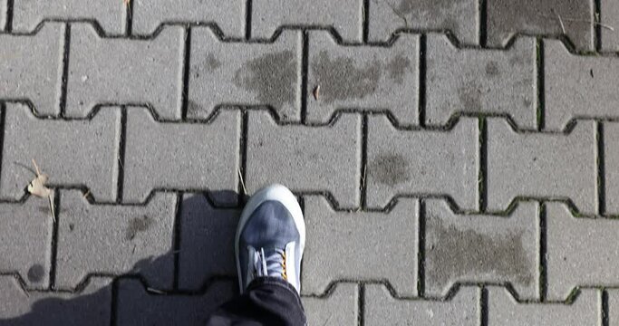 Person in dark jeans and white sneakers walks on paving slabs, top view