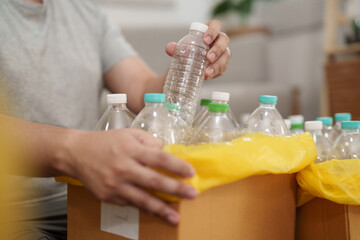 A man hand holding paper garbage bin collecting plastic bottle at his home.