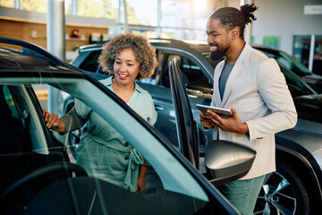 Happy black woman buying new car with help of salesman in showroom.