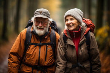 Fototapeta premium A happy older married couple, warmly dressed in winter jackets and with backpacks on their backs, are walking outdoors. The concept of a full life in retirement.