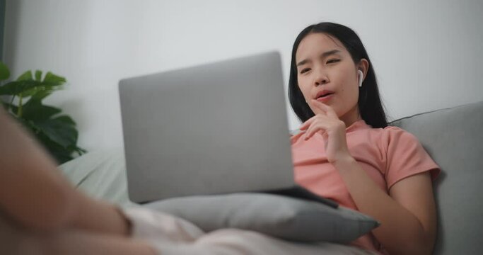 Footage of Young asian woman making video call via laptop while resting on sofa in living room,Video call meeting with team at home
