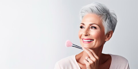 elderly gray-haired woman applying makeup with a brush in a studio background . Generative AI - obrazy, fototapety, plakaty