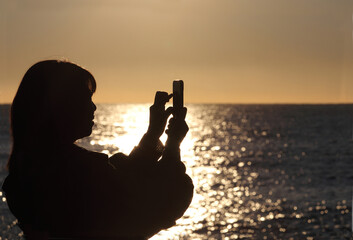 海の夕日で女性がスマホ写真を撮るシルエット