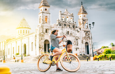 Happy tourist girl in hat on bicycle using phone on the street Granada, Nicaragua. Happy tourist...