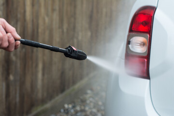 Close up photo of a man hands washes his car with a large head of water from a karcher on open air....