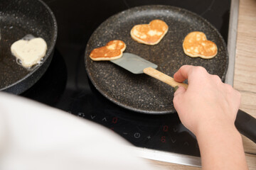 Woman cooking heart shaped pancakes on a frying pan, close-up