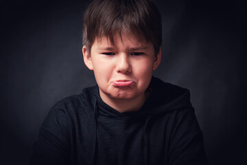 Fototapeta premium Little boy making funny sad faces on dark background. Closeup portrait of cute kid