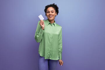 young hispanic brunette lady dressed in a green stylish shirt holds a bank plastic card on a...