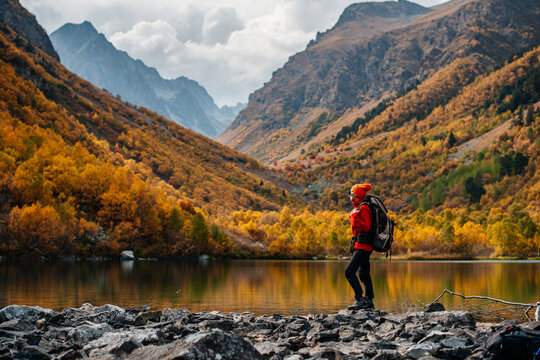 a girl with a backpack on the shore of a mountain lake in autumn