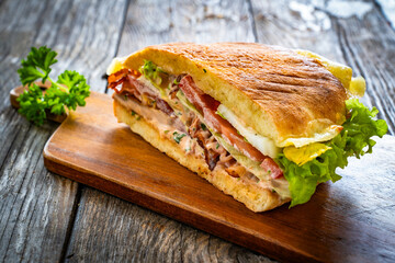 Big sandwich with grilled chicken breast and cheese and fresh vegetables on wooden table
