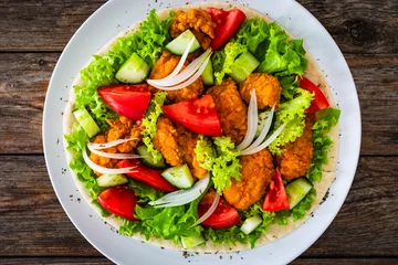 Foto auf Glas Seared chicken nuggets with vegetable salad on tortilla on wooden background  © Jacek Chabraszewski