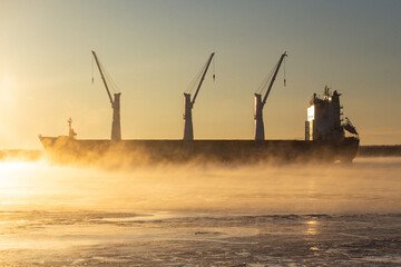  Cargo ship, ice classed bulk carrier in the ice and fog of a freezing river. High quality photo - obrazy, fototapety, plakaty