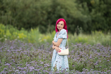 Portrait of a young beautiful girl with red hair on a forest field of phacelia.
