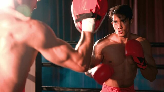 Asian and Caucasian Muay Thai boxer unleash punch in fierce boxing training session, delivering punching strike to sparring trainer, showcasing Muay Thai boxing technique and skill. Impetus