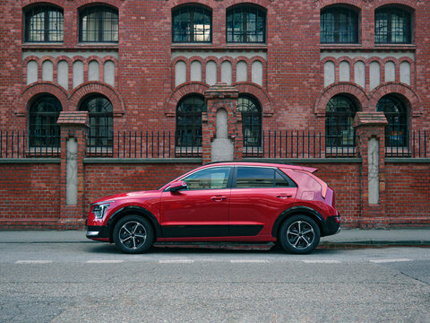 Red car, crossover type, parked in the street, side view on brick building symmetrical background