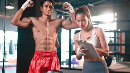 Asian female Muay Thai boxer and personal boxing trainer looking on physical progress in the gym reflecting commitment to body muscle growth and boxing performance. Impetus - Powered by Adobe