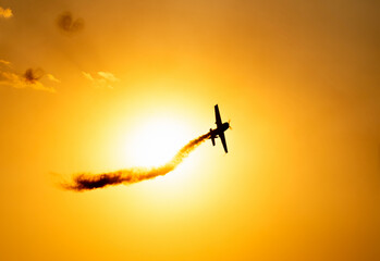 A silhouette of an aerobatic airplane flying at sunset against the crimson sky. - obrazy, fototapety, plakaty