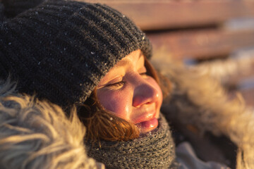 Attractive woman wearing winter clothes relaxing on the sun bed on the winter frosty sunset. Closeup portrairt. Winter solstice concept.