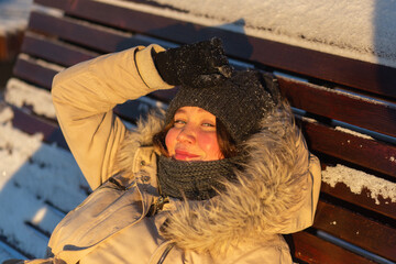 Attractive woman wearing winter clothes relaxing on the sun bed on the winter frosty sunset. Closeup portrairt. Winter solstice concept.