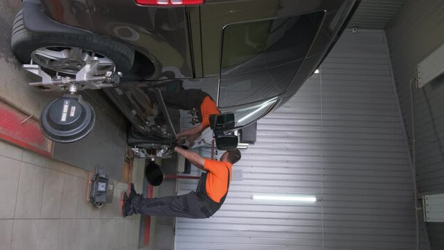 A car mechanic makes a camber in a car. Car chassis repair. Car service. Vertical video