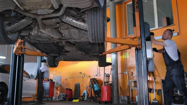 A mechanic working on a car in a car service. Professional repairman under the car. Modern car workshop