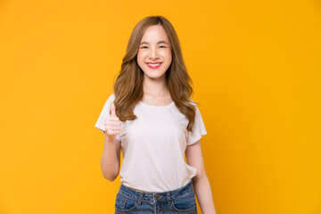 Studio shot of cheerful beautiful Asian woman in white t-shirt and showing thumbs up or like on yellow background. - obrazy, fototapety, plakaty