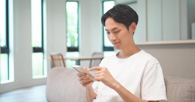ソファに座ってスマートフォンを操作する男性