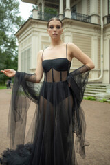 A 30-year-old girl in a black transparent revealing dress is walking on the street near her house. Style and elegance, femme fatale, photo shoot in a black dress, advertising