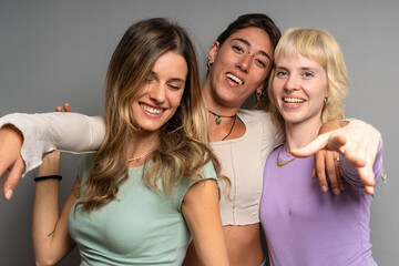 Three vibrant young women pointing and laughing together in a studio, sharing a playful and joyful...