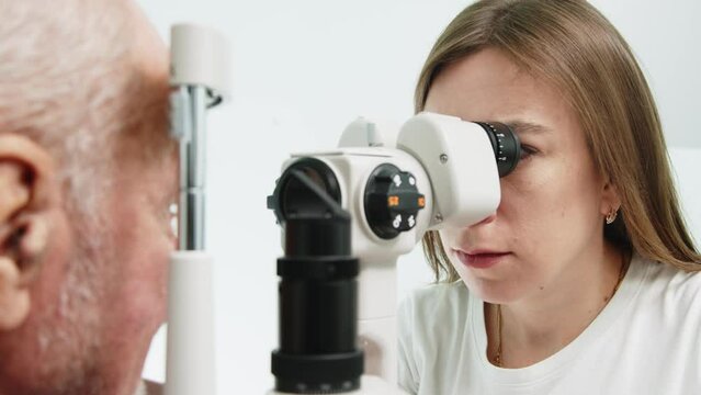 Optician doctor working with the refractometer machine. Eye exam for old man. Female ophthalmology specialist doing eye checkup. Ophthalmologist check eyesight of senior man with modern equipment. 