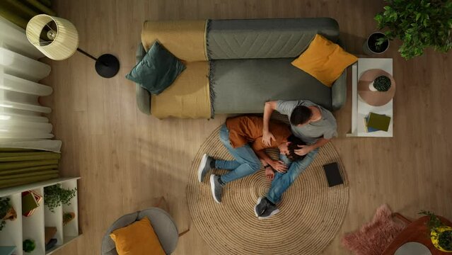 Top view capturing a homosexual male couple spending time together. One is lying on the lap of their partner who is caressing their hair. The men are talking to each other.