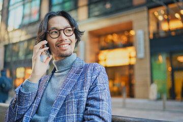 ベンチに座ってスマートフォンで電話をするジャケットを着た男性