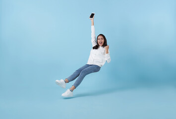 Young asian teenage girl happy hand holding mobile phone floating in mid-air isolated on blue...